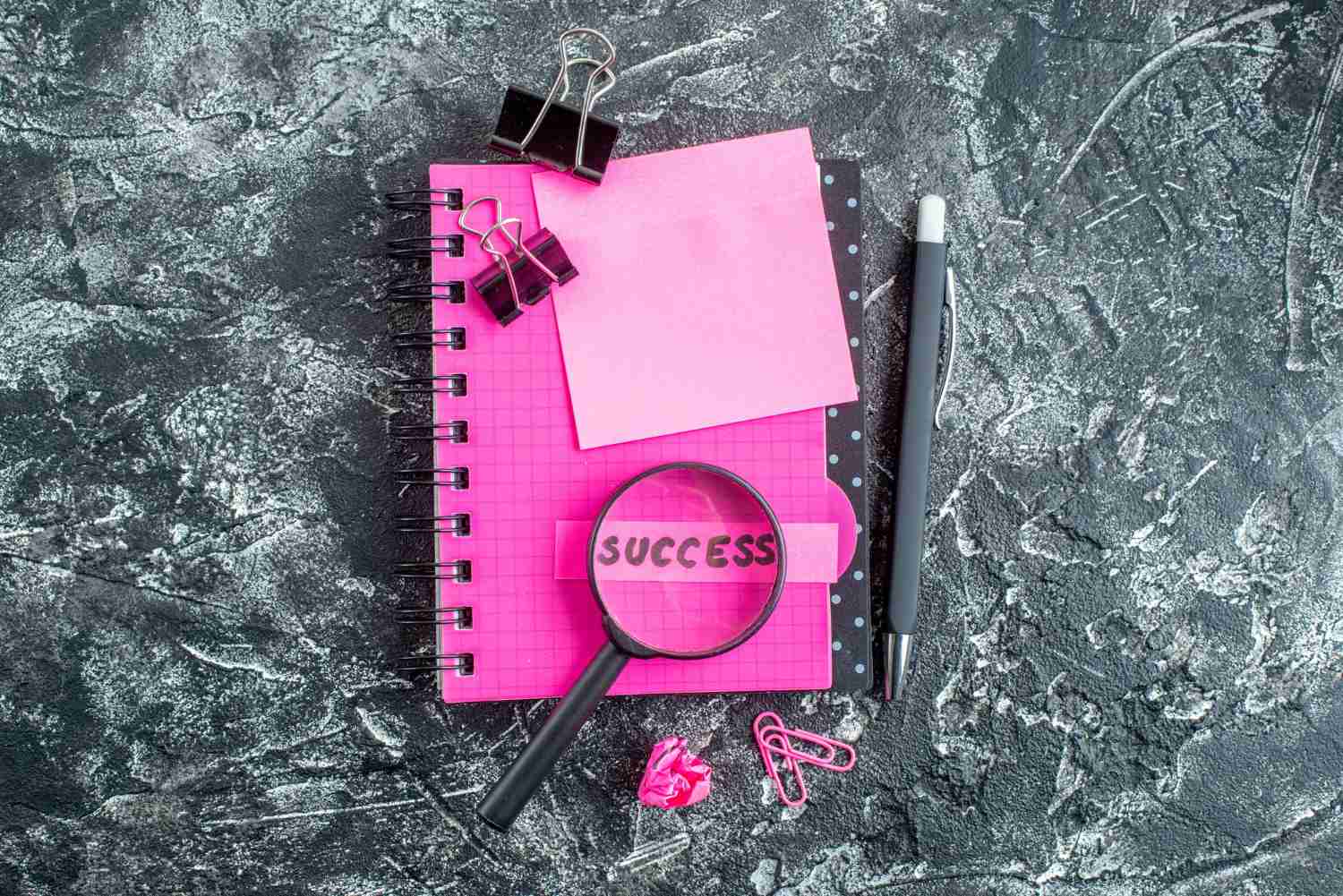 An assortment of stationery items featuring a success note pad, pen, magnifying glass and several notepads.